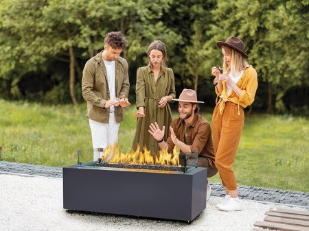 Group of young friends hang out by a fireplace, preparing for grilling at the backyard. Barbecue in close company in nature